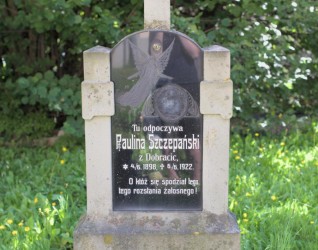 Nagrobek Pauliny Szczepańskiej z krzyżem na dwustopniowym cokole. Tablica inskrypcyjna z aniołem i tekstem po polsku, otoczona zielenią.