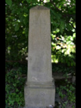 Nagrobek z obeliskiem na cokole i podstawie. Obelisk zdobi krzyż o łukowatych zakończeniach ramion i napis poniżej. Cokół ma profilowane górne krawędzie.