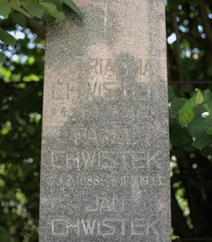 Nagrobek rodziny Chwistek z wyrytymi inskrypcjami na obelisku. Otoczony zielenią.