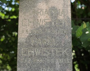 Nagrobek rodziny Chwistek z wyrytymi inskrypcjami na obelisku. Otoczony zielenią.