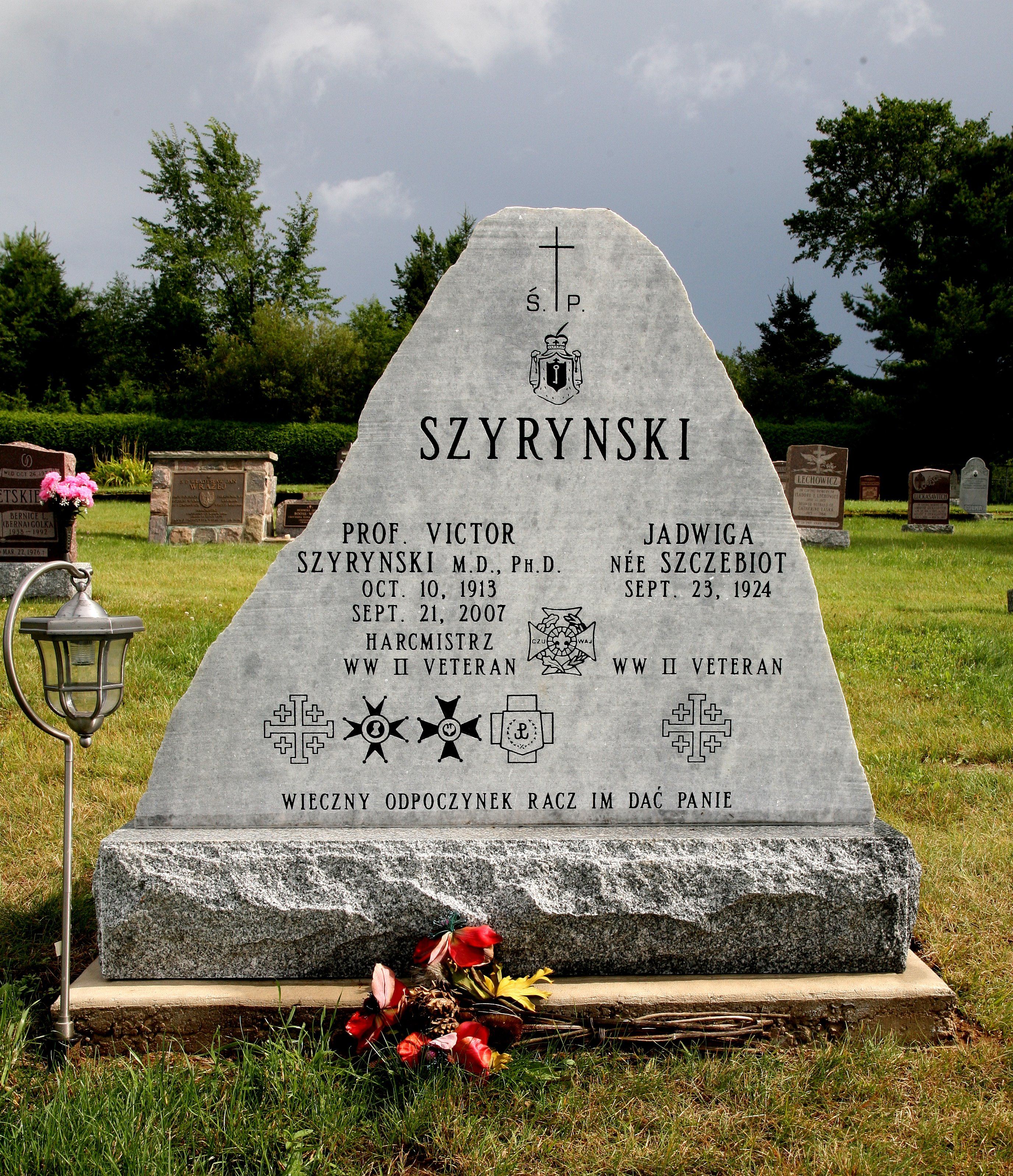Nagrobek prof. Wiktora Szyryńskiego i Jadwigi z domu Szczebiot na cmentarzu. Na kamieniu widnieją ich imiona, daty urodzenia i śmierci oraz wzmianka o statusie weterana II wojny światowej. Obok znajdują się kwiaty i latarnia.