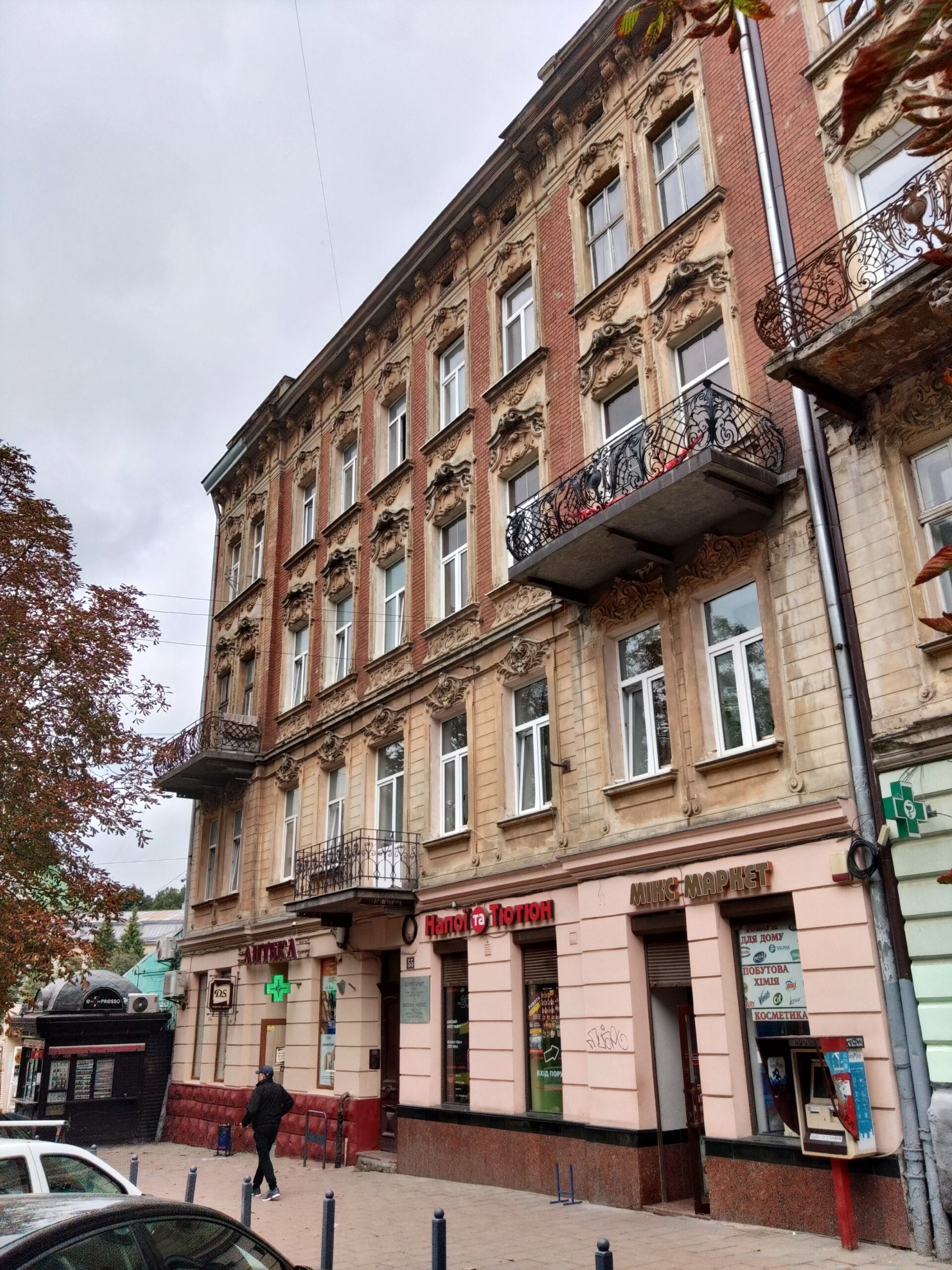 Historyczny budynek we Lwowie z ozdobną fasadą i balkonami, na parterze apteka i sklepy. Architektura odzwierciedla bogate dziedzictwo kulturowe miasta.