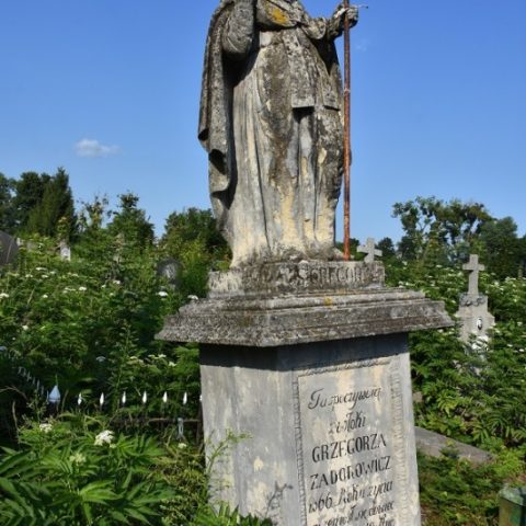 Tombe de Grzegorz Zadurowicz au cimetière de Tchernivtsi, avec une statue de Saint Grégoire. La pierre est entourée de verdure et d'autres tombes sont visibles en arrière-plan.