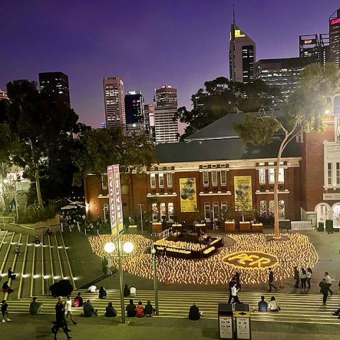 Centre culturel de Perth au crépuscule avec des marches illuminées et une cour centrale. Des personnes se rassemblent autour d'une installation lumineuse. La ligne d'horizon de la ville est visible en arrière-plan.