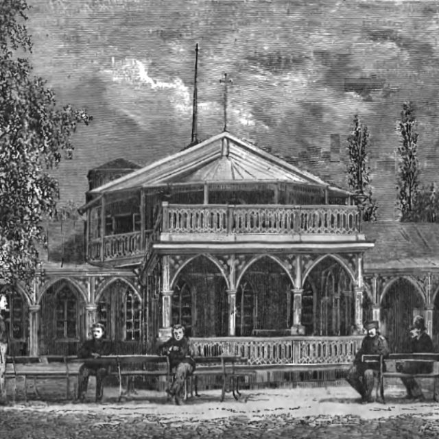 Rycina przedstawiająca zakład wód mineralnych w Druskienikach, 1877. Budynek ma dwupiętrową strukturę z łukami i balkonami. Kilka osób siedzi na ławkach przed budynkiem, otoczonym drzewami.