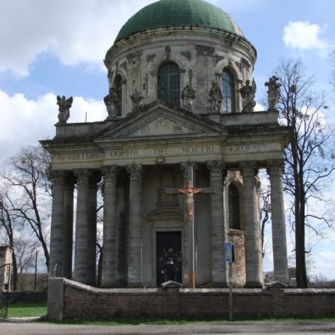Église Saint-Joseph à Pidhirtsi avec une rotonde à dôme et un portique à huit colonnes. Des statues ornent la façade, et une croix se dresse devant. Arbres et ciel nuageux en arrière-plan.