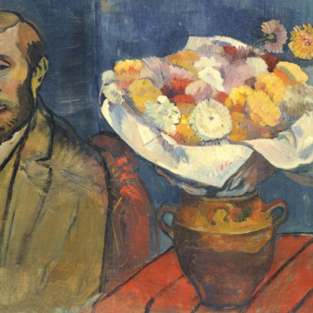 A portrait of a bearded man sitting next to a large bouquet of colourful flowers in a brown vase on a red table. The background is dark blue.