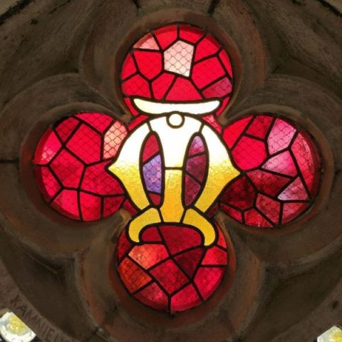 Quatrefoil en vitrail avec des pièces de verre rouges et jaunes et un monogramme 'M' au sommet de la fenêtre dans le presbytère de l'église Saint-Barthélemy à Drohobych.