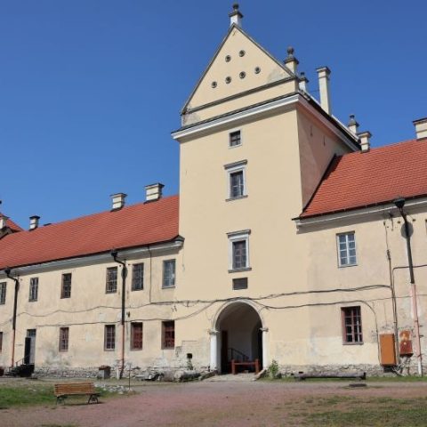 Facade of the Zhovkva Castle under renovation, showing a central tower with a triangular roof and red-tiled wings. The building has multiple windows and a large arched entrance.