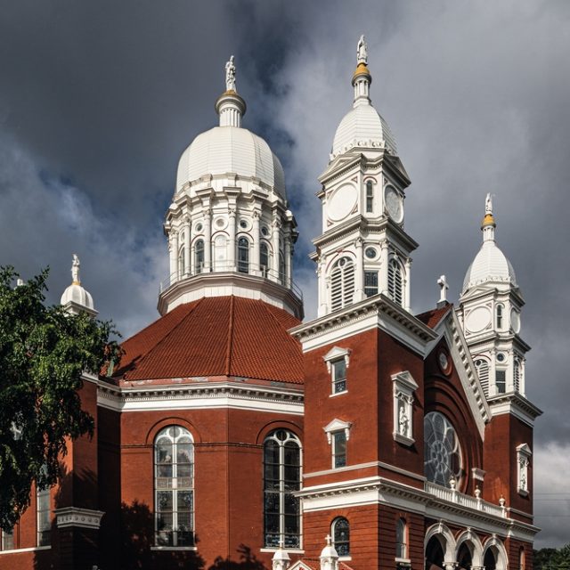 St. Stanislaus Kostka Church in Winona with its red brick facade, two white towers, and a central dome under a cloudy sky.