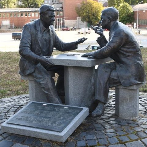 Monument représentant Henryk Sławik et József Antall senior assis à une table en pierre ornée d'un damier, plongés dans une conversation. Devant le monument, une plaque comportant des inscriptions en hongrois et en anglais. Le monument se trouve sur une esplanade circulaire pavée.