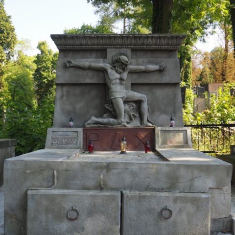Nagrobek na Cmentarzu Łyczakowskim we Lwowie z rzeźbą klęczącej postaci z rozpostartymi ramionami. Na podstawie napis 'PAX', otoczony drzewami.
