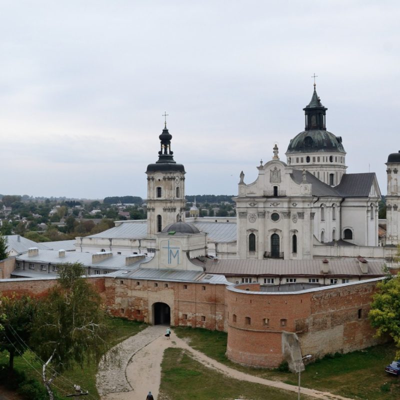 Widok na kompleks klasztorny karmelitów w Berdyczowie na Ukrainie, z widocznymi murami obronnymi i wieżami kościoła. Czerwone ceglane mury obronne są wyraźnie widoczne na pierwszym planie.
