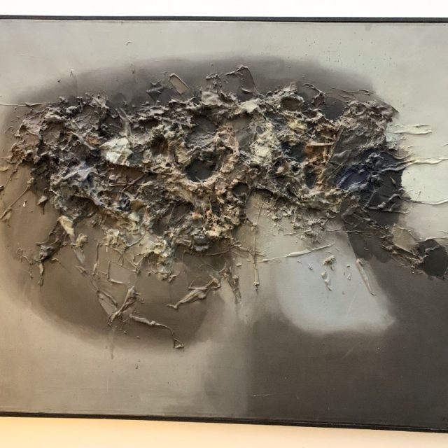 Peinture abstraite avec une surface texturée dans des tons de gris et de brun, présentant une zone centrale surélevée avec des motifs rugueux et irréguliers.