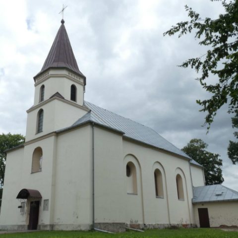 Kościół Wniebowzięcia Najświętszej Marii Panny w Łyścu, Ukraina, z wysoką wieżą i łukowatymi oknami, otoczony drzewami i pochmurnym niebem.