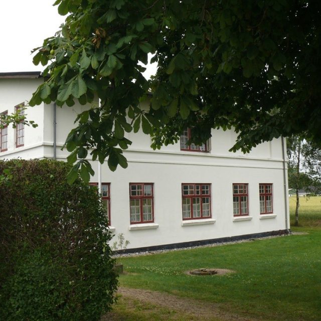 Vue extérieure du Musée de la Chambre Polonaise à Taagerup, Danemark, montrant un bâtiment blanc avec des fenêtres encadrées de rouge entouré de verdure.