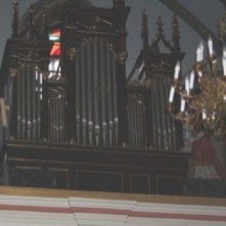 Orgue à tuyaux dans l'église de la Nativité de Saint-Jean-Baptiste à Mościska, avec des sculptures en bois ornées et un lustre au premier plan.