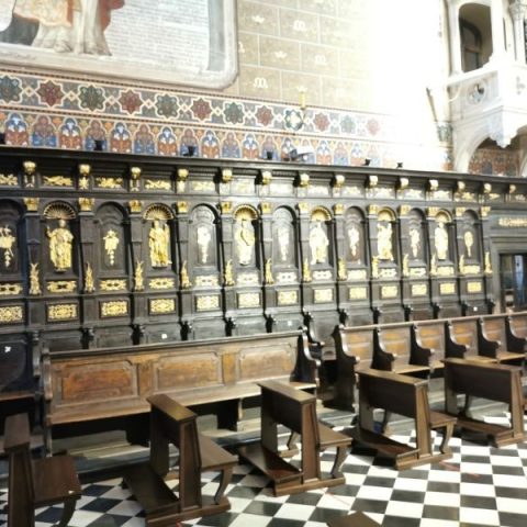 Wooden canon stalls in the presbytery of the Latin Cathedral in Lviv, featuring black paint, gilded sculptures, and decorative elements like Apostles' reliefs and clerical insignia.