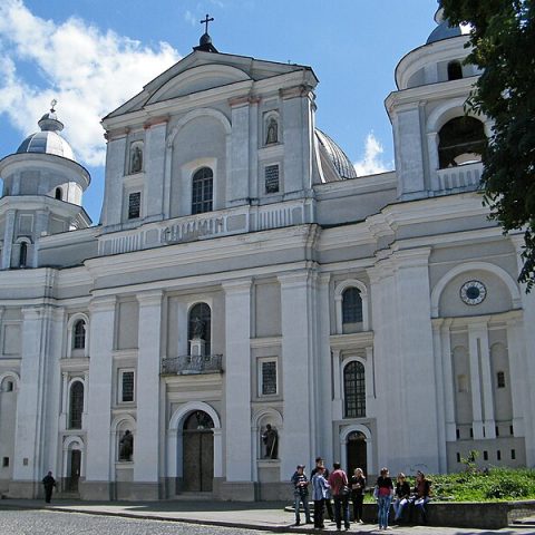 Facade of the Cathedral of Saints Peter and Paul in Lutsk, Ukraine, showing its two flanking towers and central entrance. A group of people stands in front of the building.