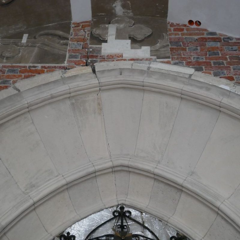 Close-up of the stone portal arch in the western porch of the Latin Cathedral in Lviv, showing cracks and brickwork above.