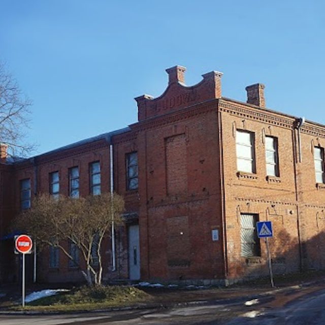 Brick building of the People's House in Khmelnitsky, Ukraine, with the inscription 'People's House' on the facade. The building has two floors, several windows and a tree nearby. A stop sign and a pedestrian crossing sign are visible.