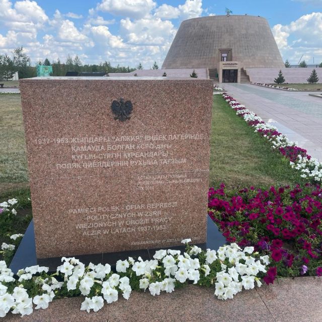 Un monument en pierre à Akmola, Kazakhstan, commémorant les femmes polonaises emprisonnées dans le camp de travail AŁŻIR de 1937 à 1953. La plaque comporte des inscriptions en russe et en polonais, entourée de fleurs.