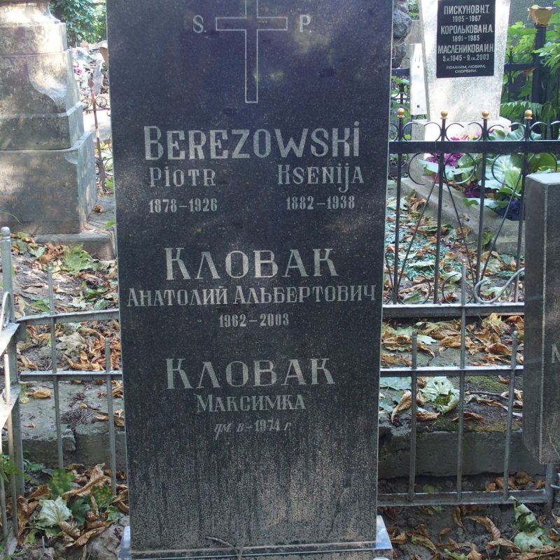 Gravestone with inscriptions for Piotr Berezowski, Ksenija Berezowski, Anatolij Al'bertovich Klovak, and Maksymka Klovak. Surrounded by a metal fence with decorative elements and fallen leaves.