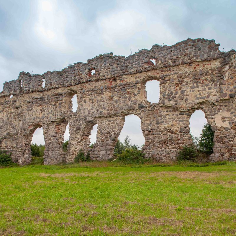 The ruins of the medieval Lais Castle, with its stone wall featuring numerous arched openings, surrounded by greenery beneath a cloudy sky.