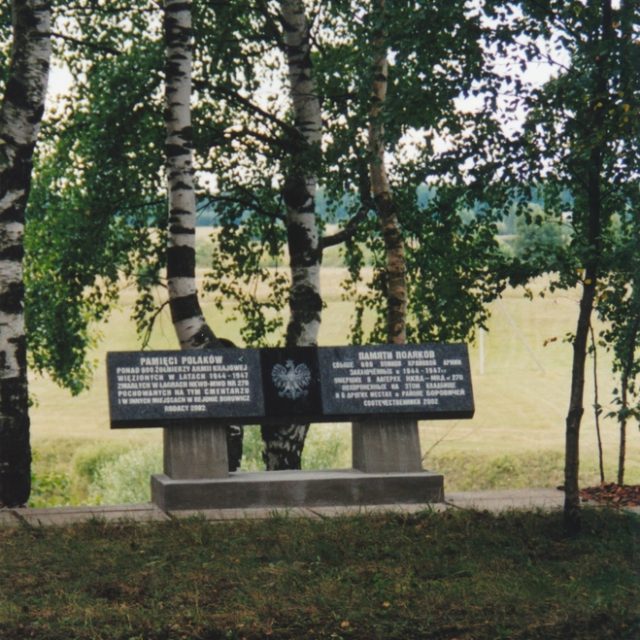 Plaque commémorative au cimetière du sous-camp de Jogła, entourée de bouleaux. La plaque commémore plus de 600 soldats de l'Armée de l'Intérieur polonaise emprisonnés et décédés dans les camps NKVD-MVD n° 270.