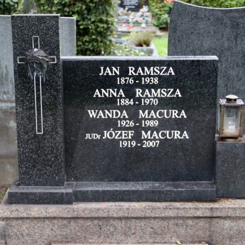 Gravestone of Ramsza and Macura families with engraved names and dates. Left side features a cross with a relief of Christ's head. A lantern is placed on the right block.