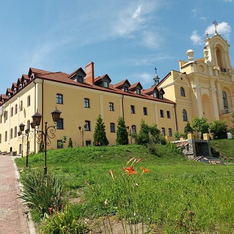 Le sanctuaire de la Visitation de la Sainte Vierge à Bołszowce, en Ukraine, avec son église jaune et son monastère situés sur une colline, entourés de verdure et de fleurs.