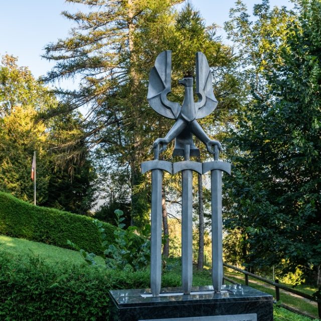 Monument in Leysin honoring soldiers of the 2nd Infantry Division. A stylized eagle rests on three swords atop a granite base, surrounded by greenery and trees.