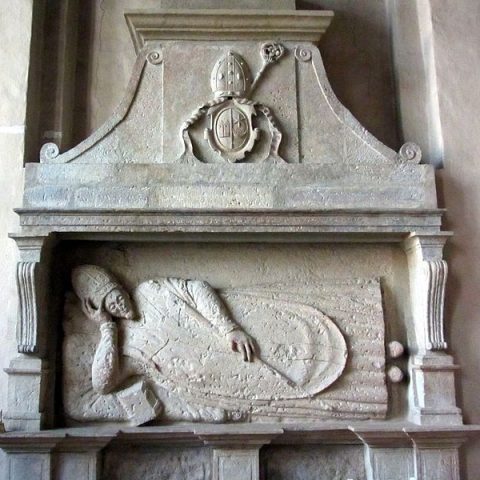 Tombeau de l'évêque Andrzej Patrycy Nidecki dans l'église Saint-Jean à Cēsis. Le relief en pierre montre l'évêque allongé en tenue épiscopale, avec un blason au-dessus.