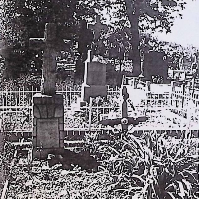Tombe marquée par une croix stylisée comme un tronc d'arbre sur un socle ressemblant à un tas de pierres. Panneau avant avec inscription gravée.