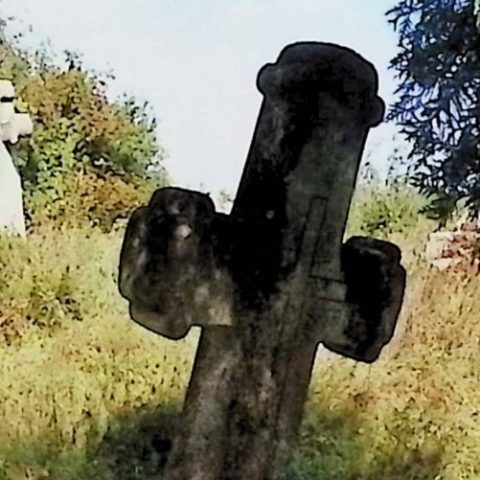 Могила, позначена хрестом на низькому постаменті з напівкруглими руками та меншим хрестом на перетині. Постамент звужується вгору, спереду напис.