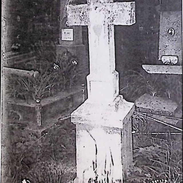 Gravestone of Aniela Piotroska with a simple cross on a pedestal. The cross features an IHS inscription and a flaming heart at the intersection of the arms. The pedestal has an engraved inscription on the front.