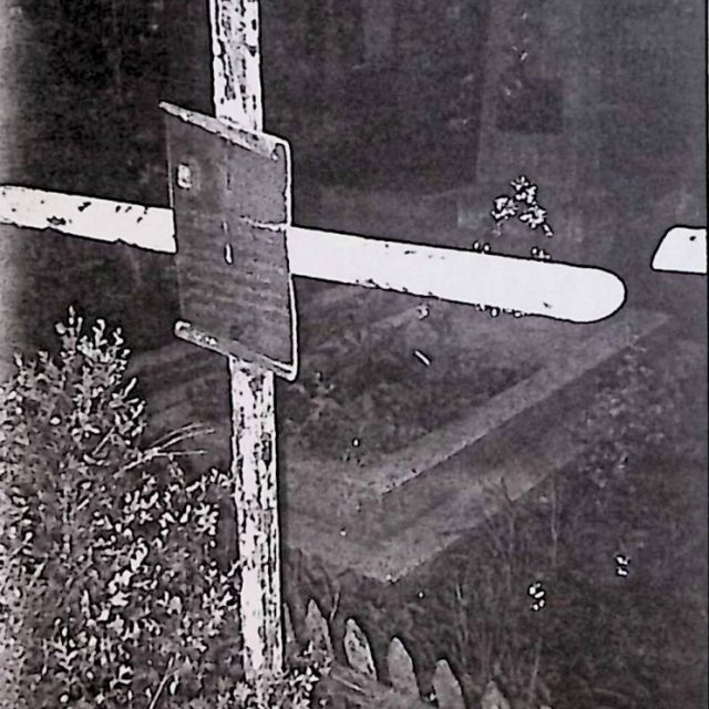 Żelazny krzyż z mosiężną tablicą z inskrypcją. W prawym górnym rogu tablicy znajduje się fotografia chłopca.