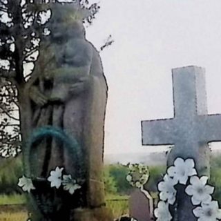 Grave marked by a statue of the Virgin Mary with Child on a two-tiered pedestal. Mary holds a scepter and the Child holds an orb. The base is adorned with acanthus leaves.