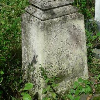 Pierre tombale de Maria Szablowska avec une croix sur un piédestal. La croix a des extrémités en trèfle et un relief du Christ. Le piédestal présente une inscription dans un cadre en arc.
