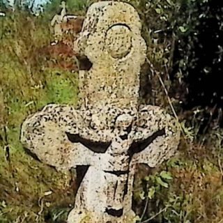 Gravestone with a cross on a rectangular pedestal. The cross has semicircular ends and a wider lower part with half-round moldings. A relief of Christ is at the intersection, with 'INRI' above and an inscription below.