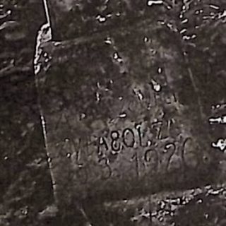 Pierre tombale avec une croix sur un piédestal. La croix a une rainure et des extrémités en trèfle avec une rosette. Une croix inscrite à l'intersection. Partie inférieure avec demi-ronds symétriques et inscription gravée.