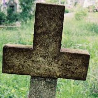 Надгробок з простим хрестом на підставці та основі, що розширюється внизу. На перетині рук вирізьблений хрест. Нижче - написаний епітафій.