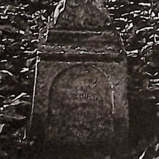 Pierre tombale d'Elżbieta Gebhart avec une croix sur un piédestal. La croix est biseautée, s'élargissant à la base, avec une petite croix à l'intersection. Le piédestal a un sommet profilé, se rétrécissant vers le haut, avec un panneau d'inscription en arc.