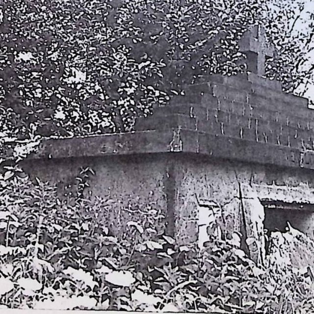Tombe rectangulaire avec une dalle rectangulaire plus large, surmontée d'un pignon à six marches avec une croix simple. Entrée avant couverte par une dalle endommagée avec poignées métalliques et blason illisible.