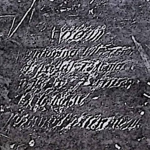 Gravestone with engraved inscription, partially worn and difficult to read, surrounded by soil and small debris.