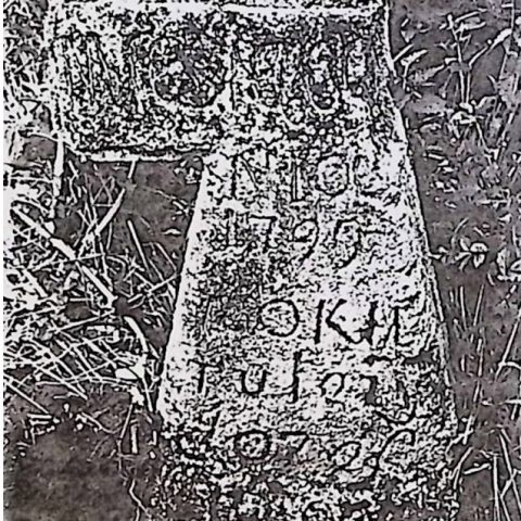 Pierre tombale en forme de croix latine avec un bras transversal cassé et une poutre verticale élargie. Le côté ouest présente une inscription et est bordé d'un cadre concave.