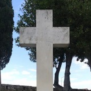 Monument to Polish defenders in Messolongi, Greece, featuring a stone cross between Greek and Polish flags, surrounded by trees.