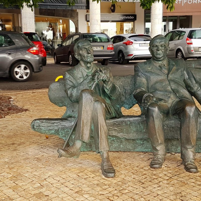 Bronze sculpture of three Polish emissaries, Jan Karski, Jerzy Lerski, and Jan Nowak-Jeziorański, seated on a bench in Estoril. A plaque with their names and dates is nearby.