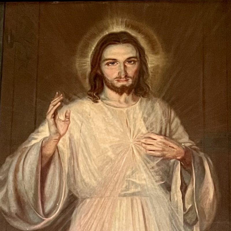 Painting 'Jesus, I Trust in You' by Adolf Hyła in Katondwe, Zambia, depicting Jesus with a raised hand and a halo, framed in ornate wood.