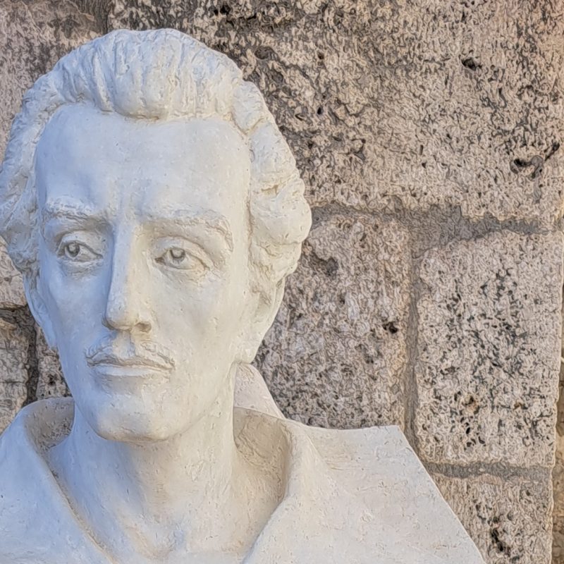 Bust of Juliusz Słowacki in Nauplion, Greece, placed in front of a stone wall.